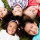 Kids laying on the grass in a circle smiling up at camera by Lice Clinics of America - Columbus, OH