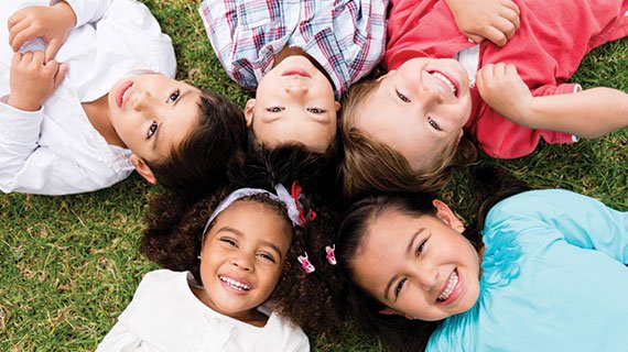 Kids laying on the grass in a circle smiling up at camera by Lice Clinics of America - Columbus, OH